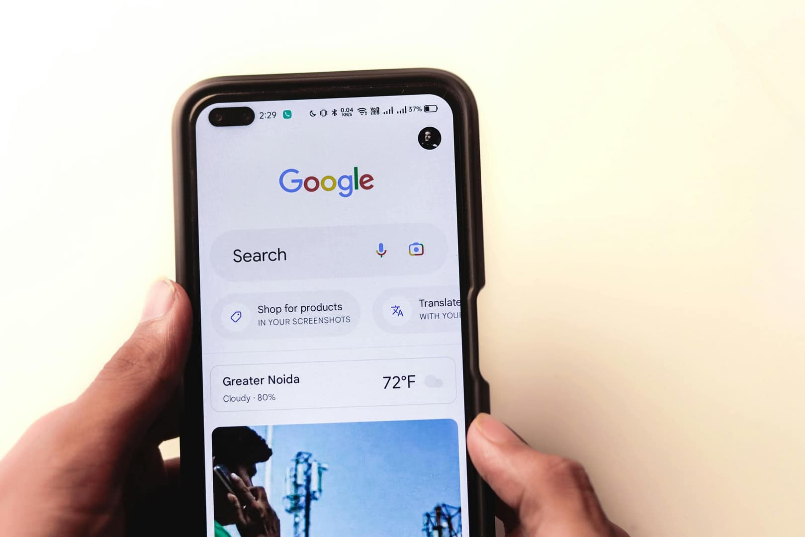 Person holding a smartphone displaying the Google search app on the home screen with the Google logo and search bar visible.